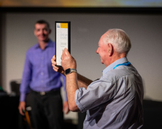 A Proud Alan Green Showing The Itsmf 2023 Conference Audience Professional Speakers Australia Kerrie Nairn Scholarship Plaque Awarded To Daryl To Help Develop Him From An Emerging Speaker To Today As A Now Full Time Professional Speaker.